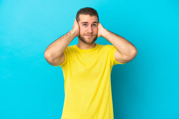 Young handsome caucasian man isolated on blue background frustrated and covering ears - Fotó, kép