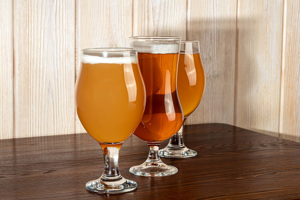 Bicchieri con diversi tipi di birra artigianale su un bar in legno. In bicchieri e bottiglie. Noci e cracker sul tavolo. Su uno sfondo scuro. - Foto, immagini