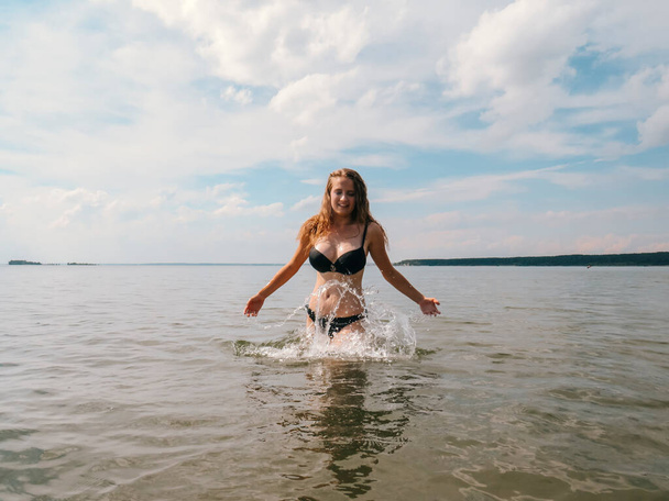 Beautiful young woman with a slender figure on the background of water splashes on the shallow waters of the sea beach on a hot summer day, the concept of beach holidays, sun tanning, swimming - Fotó, kép