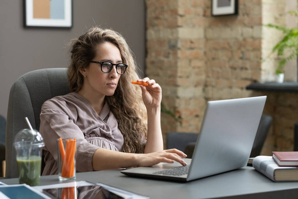 Mulher de negócios grávida com cenoura olhando para a tela do laptop - Foto, Imagem