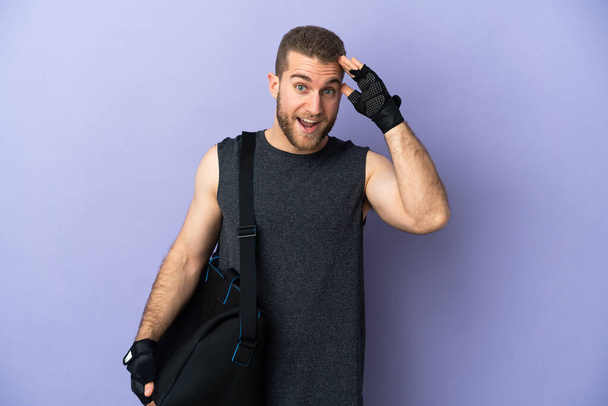Mladý sportovní muž se sportovní taškou izolované na bílém pozadí s překvapivým výrazem - Fotografie, Obrázek