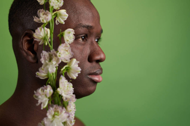 Πλευρική άποψη του κεφαλιού του μαύρου άνδρα και λευκά λουλούδια - Φωτογραφία, εικόνα