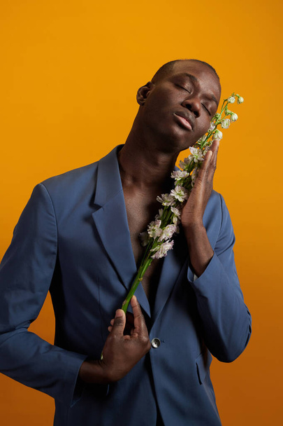 Африканский мужчина в синей куртке держит белые цветы на лице - Фото, изображение