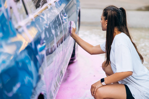 Brunette with two pigtails with a sponge washes the side of the car - Fotoğraf, Görsel