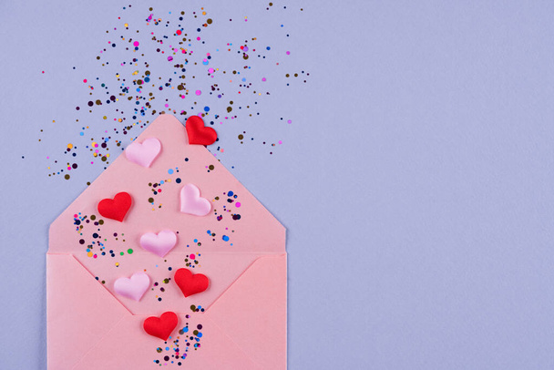 День Святого Валентина святковий фон. Рожевий конверт з червоними серцями та різнокольоровими конфетті на пастельно-фіолетовому тлі з пробілом для копіювання. Плоска композиція, вид зверху
 - Фото, зображення