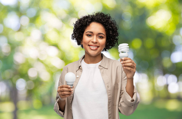 smiling woman holding lighting bulbs over green - Foto, afbeelding