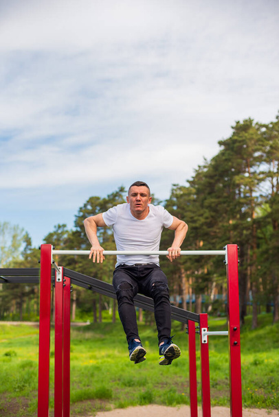 Caucasian man pulls himself up on a horizontal bar on a sports ground. - Foto, Imagen