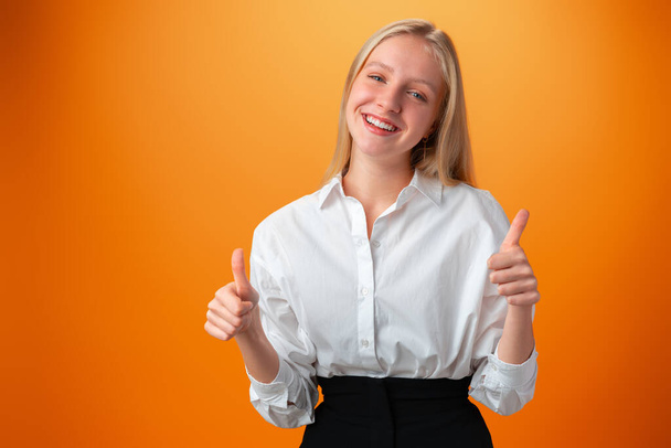 Teen girl making thumb up gesture against orange background - Fotó, kép