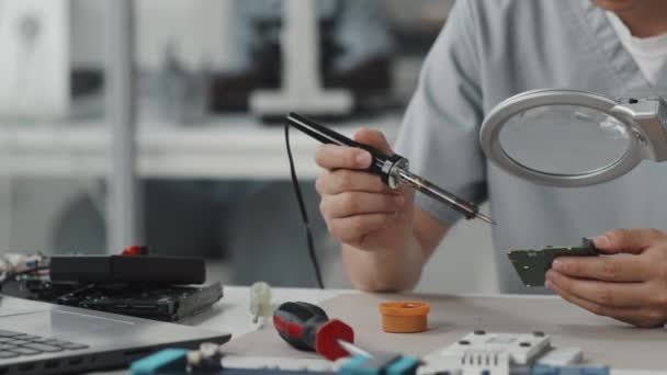 Primer plano del técnico de laboratorio femenino usando lupa de escritorio mientras se repara la placa de circuito informático con soldador - Metraje, vídeo