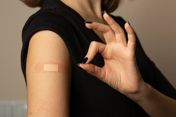 Woman with adhesive plaster on her arm after taking vaccine showing ok sign by fingers - Photo, Image
