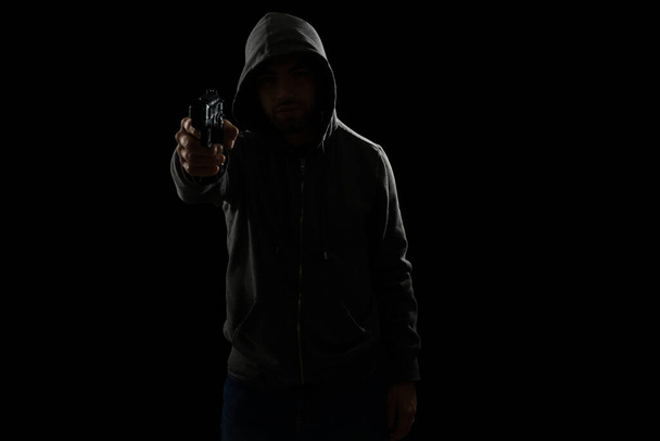 Roubo à mão armada. Ladrão apontando uma arma e olhando para a câmera contra um fundo preto escuro - Foto, Imagem
