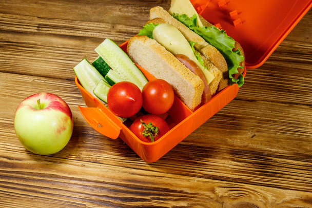 Apple and lunch box with sandwiches and fresh vegetables on a wooden table - Photo, Image