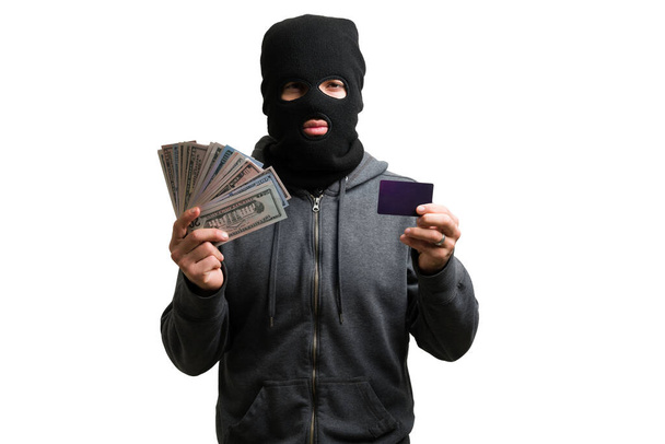 Tajemniczy zamaskowany człowiek i złodziej pokazujący skradzione pieniądze i kartę kredytową na białym tle - Zdjęcie, obraz