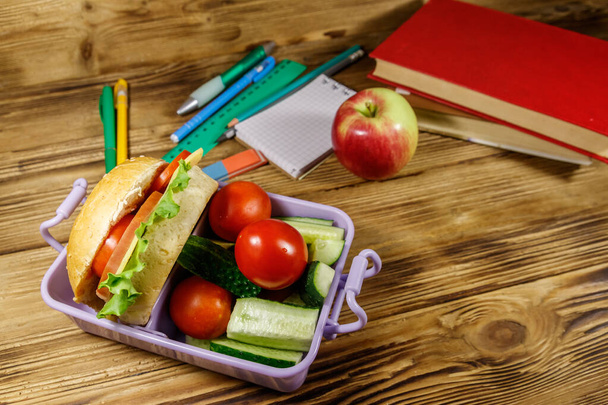 Okul konseptine geri dönelim. Okul gereçleri, kitaplar, elma ve beslenme çantası. Hamburgerler ve taze sebzeler ahşap bir masada. - Fotoğraf, Görsel