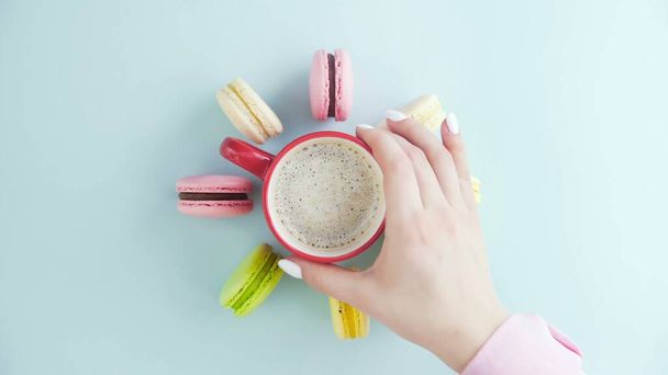 Draufsicht auf bunte französische Macarons-Kekse und eine Tasse Kaffee auf pastellblauem Hintergrund - Foto, Bild