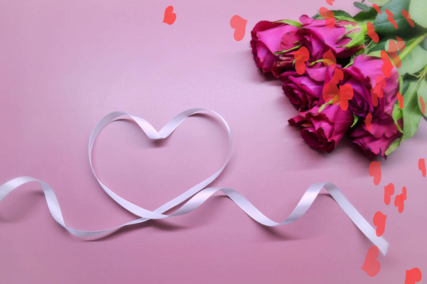 Kytice z rudých růží leží na růžovém pozadí. Srdce z bílé stuhy. Se srdcem ve tvaru bokeh - Fotografie, Obrázek