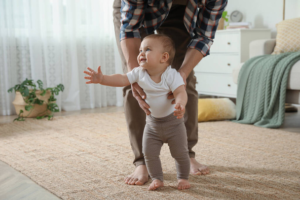 Father supporting his baby daughter while she learning to walk at home - Photo, Image