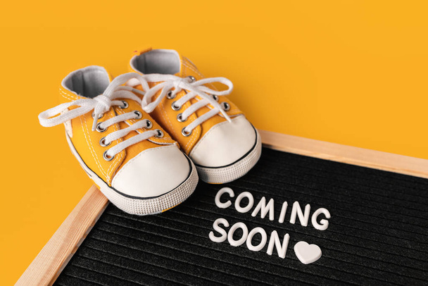 Tiny baby's sneakers and a board with the inscription "coming soon". Pregnancy concept and expecting baby - Photo, Image