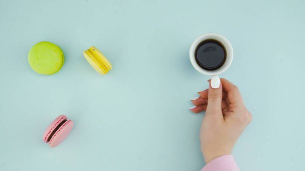 Draufsicht auf bunte französische Macarons-Kekse und eine Tasse Kaffee auf pastellblauem Hintergrund - Foto, Bild