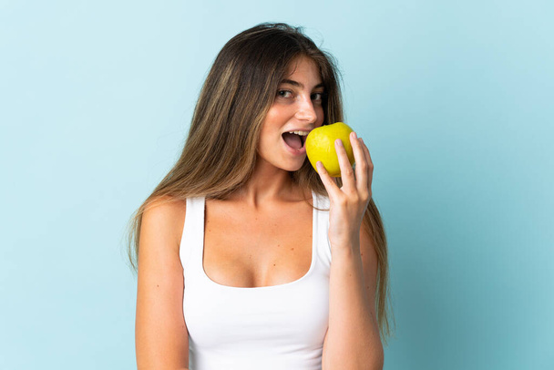 Молодая белая женщина на голубом фоне ест яблоко - Фото, изображение