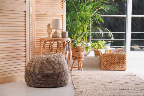Stylish knitted pouf, wicker furniture and beautiful houseplants in room. Interior design - Foto, Bild