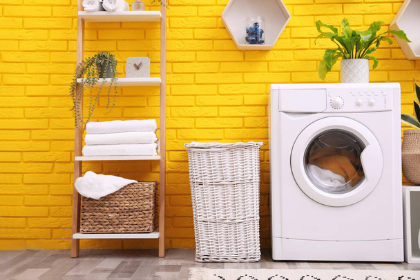 Laundry room interior with modern washing machine near yellow brick wall - Фото, изображение