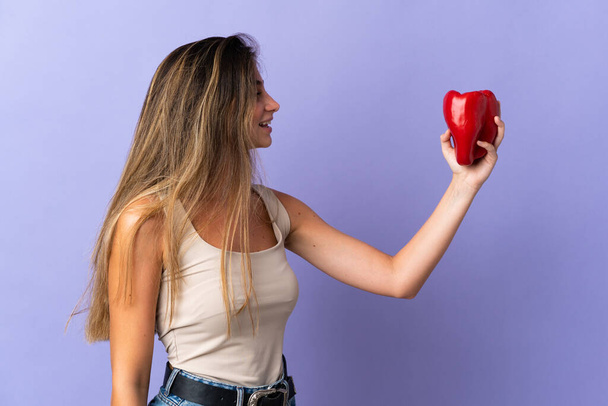Giovane donna che tiene un pepe isolato su sfondo viola con espressione felice - Foto, immagini