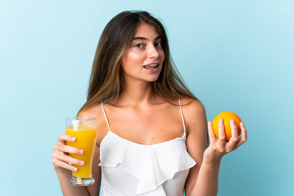 Молода біла жінка ізольована на синьому фоні, тримає апельсиновий і апельсиновий сік
 - Фото, зображення