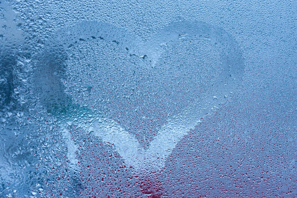 Detailní záběr na milostnou srdeční kondenzaci nápis přes zpocené okenní sklo pozadí. Valentýnský koncept tvůrčího symbolu. Ruka kreslí srdce na zamlžené okno - Fotografie, Obrázek