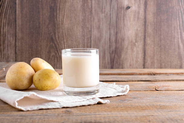 Vegaaninen perunamaito lasissa ja perunan mukulat ruskealla puupohjalla. Sulje se. Kasvipohjainen vaihtoehtoinen maidonkorvike ja laktoositon, Trendikäs terveellinen kasvis- ja vegaanijuomakonsepti - Valokuva, kuva