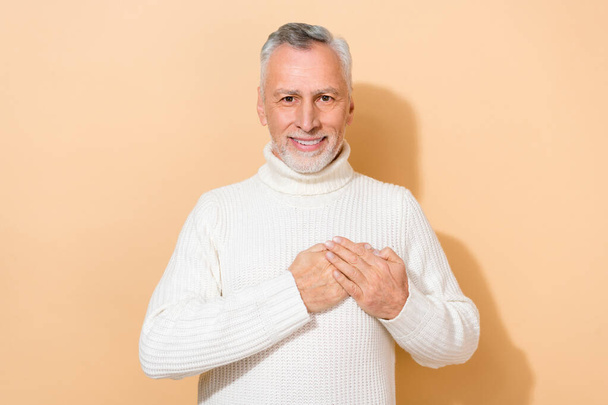 Portrait of attractive cheerful kind grey-haired man touching heart feelings isolated over beige pastel color background. - Foto, afbeelding
