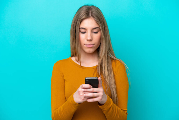 Mladá běloška žena izolované na modrém pozadí pomocí mobilního telefonu - Fotografie, Obrázek