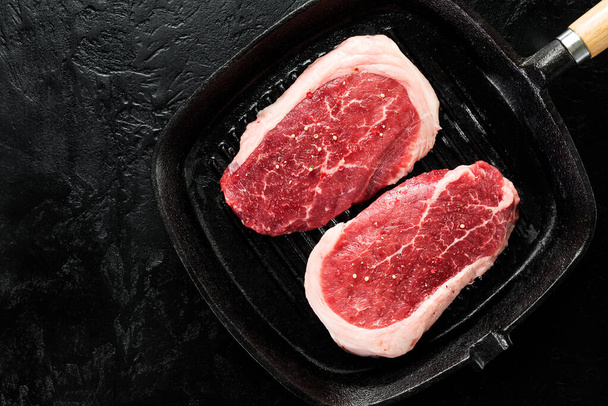 Raw Steak Ribeye Black Angus in grill pan on a black stone background. Top view. - Foto, Imagem