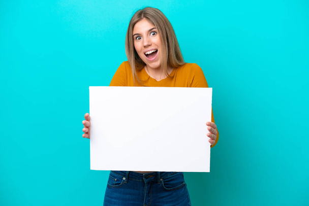 Young caucasian woman isolated on blue background holding an empty placard with happy expression - Foto, afbeelding
