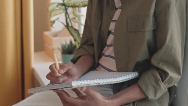 Обрезанный снимок неузнаваемого школьника в повседневной одежде, делающего домашнее задание в блокноте - Кадры, видео