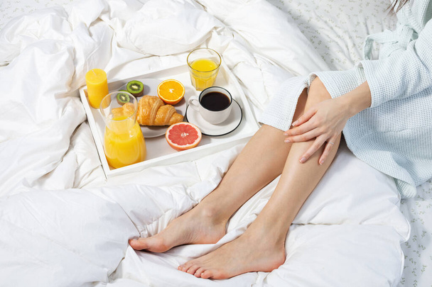 Fiatal nő az ágyban reggelizés, kávé, croissant és narancslé. - Fotó, kép