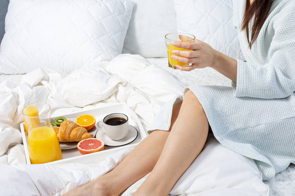Молода жінка їсть сніданок з кавою, круасанами та апельсиновим соком у ліжку
. - Фото, зображення