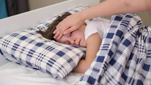 caring mother holding head on sick son forehead. Children healthcare concept. Sad little boy lies on the bed. - Foto, Bild