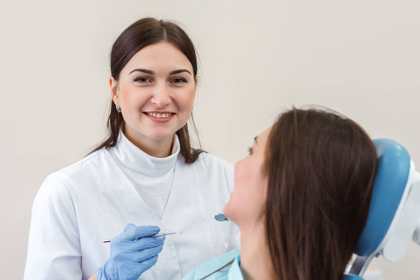 Young female patient visiting dentist office.Beautiful woman with healthy straight white teeth sitting at dental chair with open mouth during oral checkup while doctor working at teeth - Fotó, kép