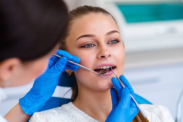 Beautiful young woman doing tooth examination in the dental office. Portrait of smiling girl on a dental chair in dentistry - Photo, Image