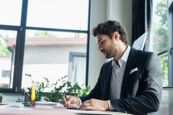 stylish businessman in black blazer writing at workplace in office - 写真・画像