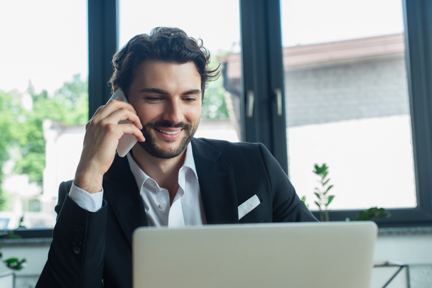 tyylikäs ja onnellinen liikemies puhuu matkapuhelimella toimistossa - Valokuva, kuva