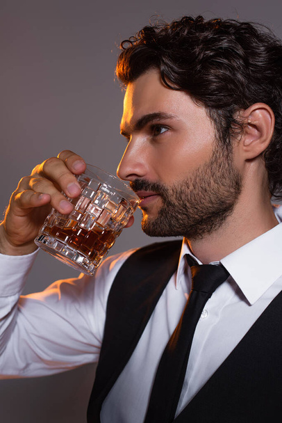 brunette man in white shirt and black tie drinking whiskey isolated on grey - Fotó, kép
