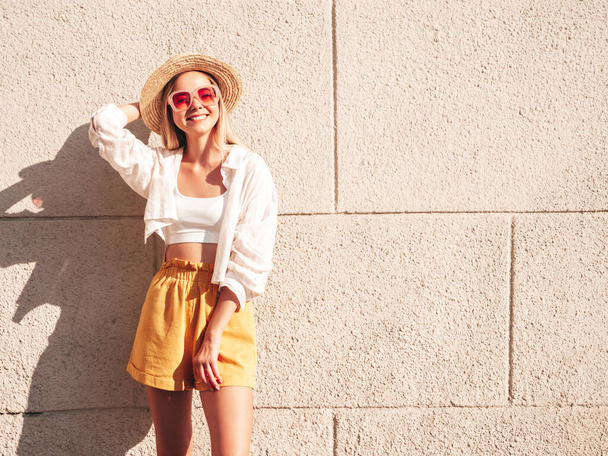 Young beautiful smiling hipster woman in trendy summer colourful clothes.Sexy carefree woman posing near white wall in the street at sunset in hat. Positive model outdoors.Happy and cheerful - Φωτογραφία, εικόνα