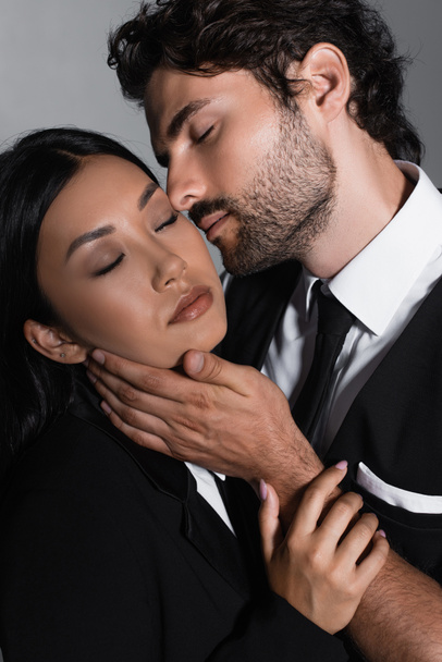 eleganter Mann küsst sinnliche asiatische Frau isoliert auf grau - Foto, Bild
