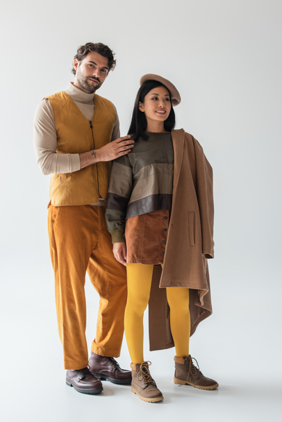 trendy man op zoek naar camera in de buurt van aziatische vrouw in baret en gele panty op grijs - Foto, afbeelding