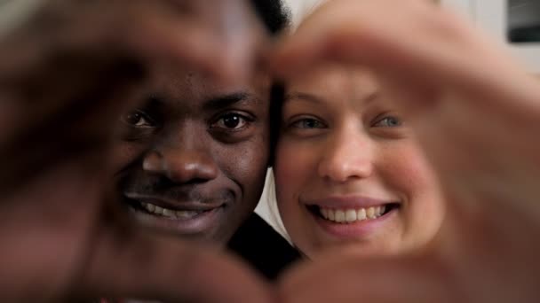 Close up sorrindo multiétnico casal rostos olhando através de dedos unidos coração - Filmagem, Vídeo