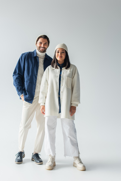 full length view of interracial couple in trendy white and blue clothes on grey background - Φωτογραφία, εικόνα