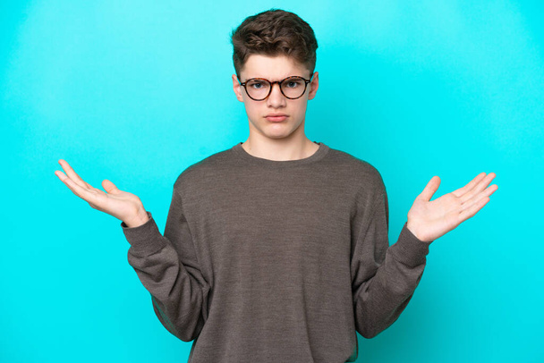 Teenager Russian man isolated on blue background having doubts while raising hands - Fotoğraf, Görsel