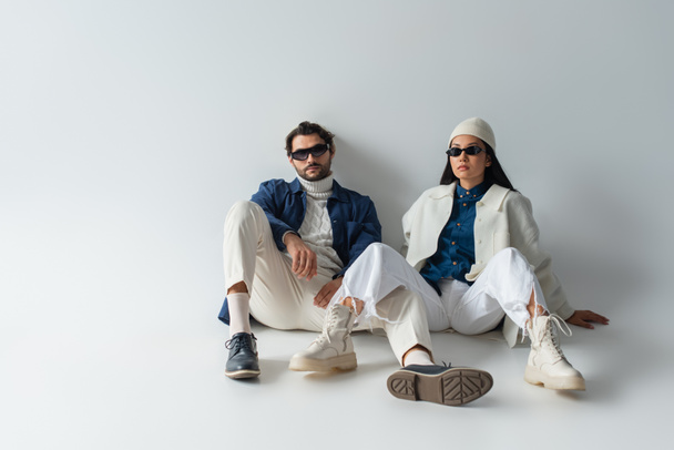 full length view of interracial couple in white and blue clothes sitting on grey - Photo, Image